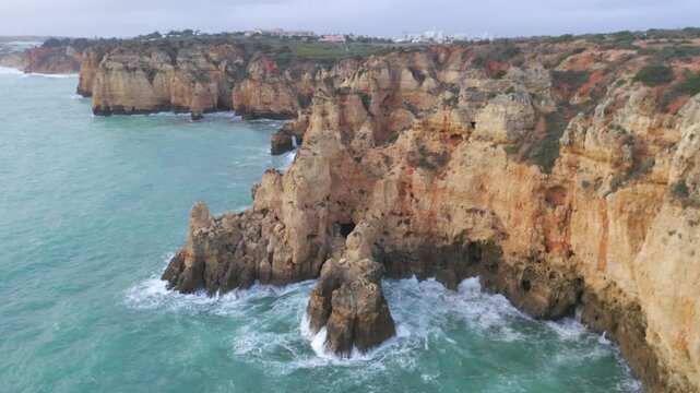 Aerial approaching of Rugged Coastal Cliffs of the Algarve in Portugal among Turquoise Waters. High quality 4k footageAerial approaching of Rugged Coastal Cliffs of the Algarve in Portugal among