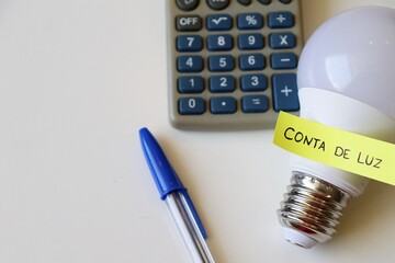 Conta de Luz (electricity bill in Portuguese) post-it reminder stuck on a light bulb and calculator. Electricity bill in Brazil concept.