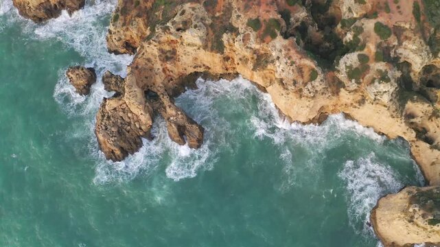 Top down aerial over Algarve coastal cliffs and waves crashing on rocks in Ponta da Piedade