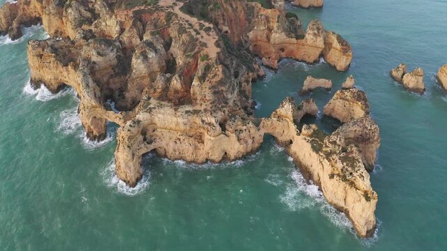 Aerial approaching of Rugged Coastal Cliffs of the Algarve in Portugal among Turquoise Waters