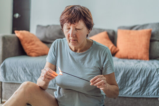 Older woman lighting an aromatic incense stick at home, creating a calming and peaceful atmosphere. Wellness, mindfulness and self-care concept, reflecting relaxation, ritual, comfort and serene