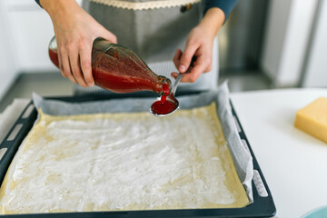 Young woman spreading tomato sauce on pizza