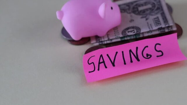 Un primer plano de un cerdo de color rosado con una nota con la palabra ahorros y rodeado de dinero en un fondo de color amarillo claro