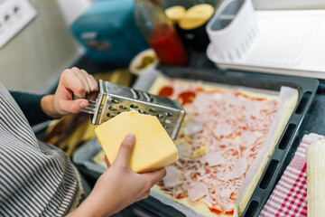 Close-up of hands grating cheese on pizza
