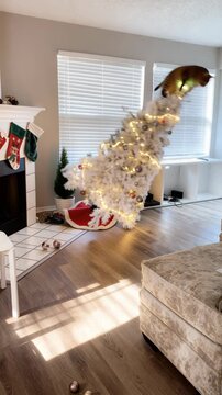 cat knocks over a Christmas tree, a funny incident, white Christmas tree with lights and decorations sits by fireplace with cat, creating cozy and joyful winter scene indoors, Christmas, family, holid
