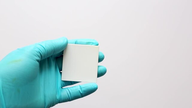 A scientist&rsquo;s hand showing a small Thin Layer Chromatography (TLC) plate cut from a larger sheet for separating chemical compounds