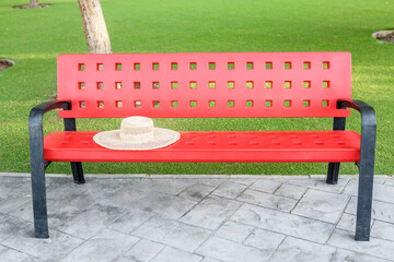 Red bench with straw hat in lush green park setting