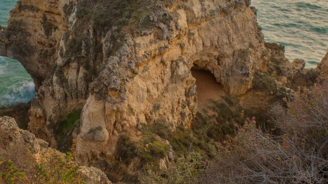 Detailed tracking timelapse of vibrant blue ocean waves lapping at dramatic coastal arch rock formations in Ponta da Piedade, Algarve, Portugal