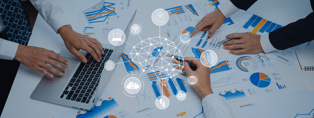 A business team collaborates over data analysis with laptops and charts in a modern office. Visuals include various graphs and statistical information indicating marketing strategies. Trope