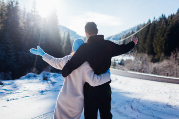Obraz premium Back view of happy couple in love hugging on background of winter Carpathian mountains by car. Travelling by auto