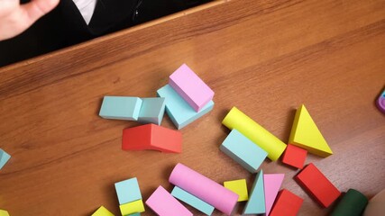 Childs hands aggressively smashing soft foam block tower on table, bright pieces flying apart, emotional release during playtime, useful for psychology blogs, parenting topics and kids therapy content