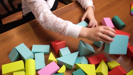 Little girls hands arranging colorful foam blocks on wooden table, building simple structure during quiet playtime, early learning scene for preschool materials, toy brands and parenting blogs - Powered by Adobe