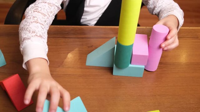 Little girls hands building a wobbly tower from soft pastel blocks on wooden table, shapes constantly collapsing, playful trial and error moment for early education, parenting blogs and toy brands