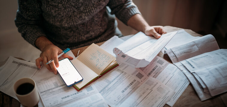 Close-up of men's hands with a calculator and utility bills. The concept of rising prices for heating, gas, and electricity. Lots of utility bills and hands with a calculator and a notebook