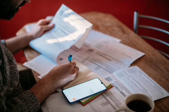A man pays utility bills online using a QR code in an app using a smartphone in the kitchen. Close-up of hands, phone, and bills.