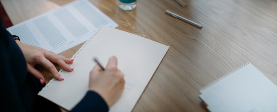 Close-up of hands with a notebook on the exam table. A student takes a test at his desk, writes a task in a notebook in the classroom
