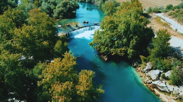 View of Manavgat Waterfall from above in the National Park on a sunny summer day. Unique azure watercolor color with splashes. A wide stream of water falls from a low height. Antalya, Dron, 4K