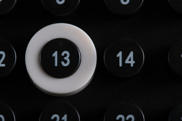 Close up view of black calendar showing number 13 highlighted with white ring among surrounding numbered buttons.