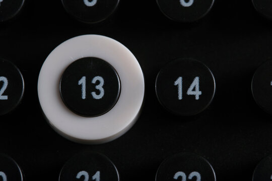 Close up view of black calendar showing number 13 highlighted with white ring among surrounding numbered buttons.