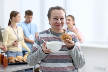 Volunteers giving food to homeless people in shelter, focus on senior woman with meal
