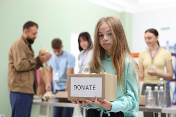 Obraz premium Volunteers helping homeless people in shelter, focus on girl with box of donations