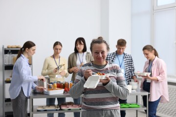 Volunteers giving food to homeless people in shelter, focus on senior woman with meal