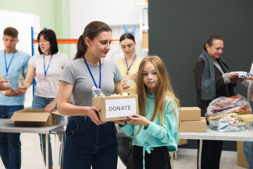 Volunteers helping homeless people in shelter, focus on volunteer and girl with box of donations