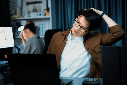 Sales manager working on desk with stretching body with arm ache at over late night time at modern home office with secretary sitting back investing dynamic stock market on project database. Infobahn. - Powered by Adobe