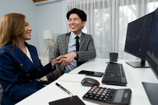 Successful smiling Asian business partners hands checking together in profitable project job in stock exchange database on pc wearing in formal suit at modern home office at side view image. Infobahn.