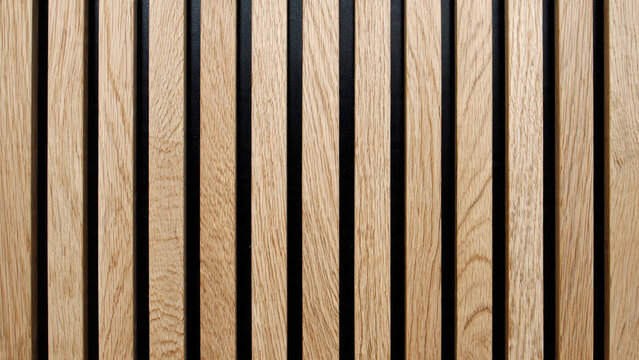 Close-up of modern acoustic wood paneling featuring light vertical timber slats on a dark background, creating a stylish textured wall design.