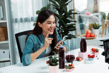 Smiling young beautiful Asian reviewing tasty mixed strawberry and cherry juice detox drinks,...