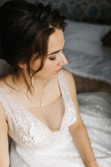 Portrait of a bride sitting indoors in her wedding dress. She looks at the camera with a calm, confident expression. Soft light highlights the lace details, veil, and floral bracelet, creating 