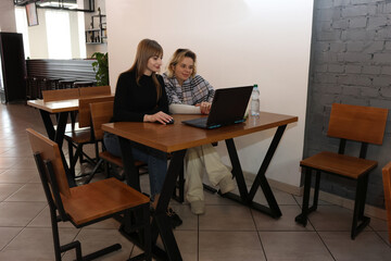 Fototapeta premium Two women working on a laptop while sitting at a table in a cafe