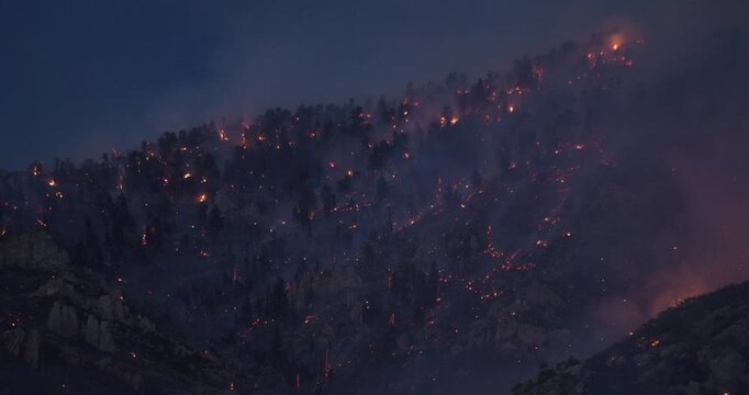 Burning and smoking rocky mountain side at dusk