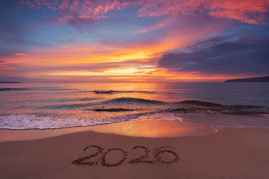 Scenic sunrise over the sea horizon and beach text Happy New Year 2026 on the sand