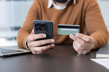 Man using a mobile phone and credit card, performing an online transaction or mobile payment for e-commerce, banking, or digital shopping from a modern office setting