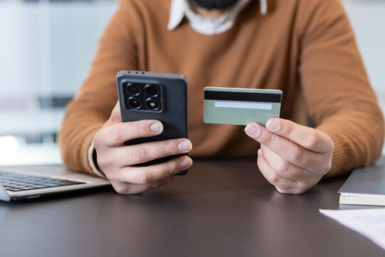 Man using a mobile phone and credit card, performing an online transaction or mobile payment for e-commerce, banking, or digital shopping from a modern office setting