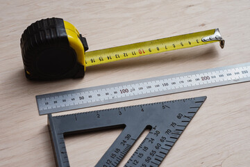Measuring tape with construction square and metal rulers arranged on a wooden surface. Concept precision and professional carpentry tools for woodworking and technical measurement themes.