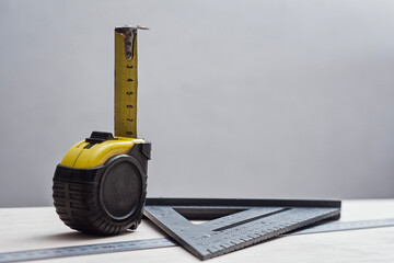 Measuring tape with construction square and metal rulers arranged on a wooden surface. Concept precision and professional carpentry tools for woodworking and technical measurement themes.