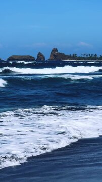 The sea in Jember, East Java. Indonesia. Watu Ulo beach with dark sand, mountains and coral rocks towering above the beach. The raging blue Indian ocean on a sunny day. 4К