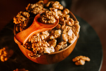 Peeled walnuts in a wooden bowl with a spoon on a dark surface