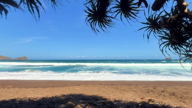 The sea in Jember, East Java. Indonesia. Watu Ulo beach with dark sand, mountains and coral rocks towering above the beach. The raging blue Indian ocean on a sunny day. 4К