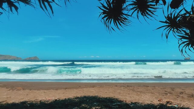 The sea in Jember, East Java. Indonesia. Watu Ulo beach with dark sand, mountains and coral rocks towering above the beach. The raging blue Indian ocean on a sunny day. 4К	