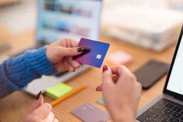 A person holds a payment card near a laptop, ready to make an online purchase.