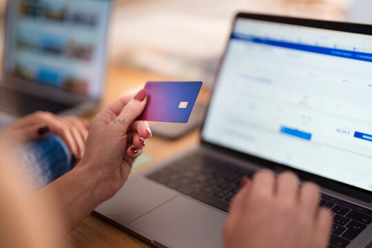 A person holds a payment card while typing on a laptop, engaging in online transactions.