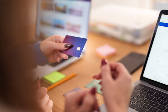 A person holds a credit card and uses a laptop to make an online purchase.