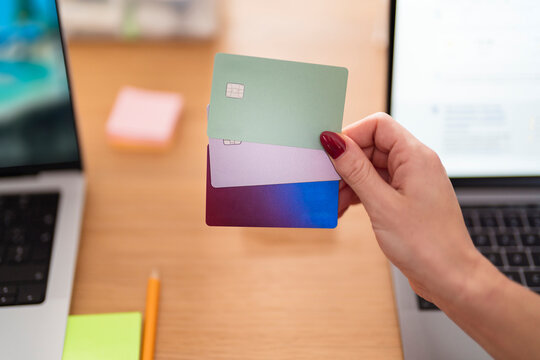 A person holds three credit cards, one green, one purple, and one blue, in front of a laptop, symbolizing financial management and online transactions.