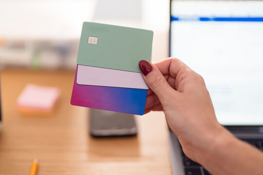 A person holds multiple payment cards, including Visa and Mastercard, near a laptop, suggesting online transactions or financial management.