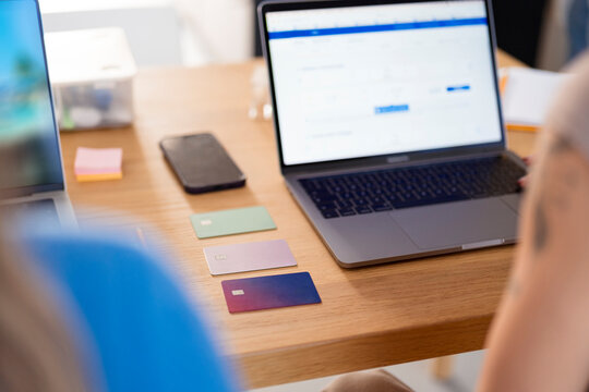 A person uses a laptop and credit cards on a wooden desk, with a smartphone and sticky notes nearby, suggesting online transactions or financial planning.