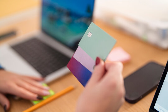 A person holds multiple credit cards near a laptop and smartphone, suggesting online transactions or financial management.